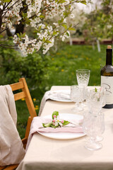 Stylish table setting with beautiful spring flowers, wine, plates and glasses in garden