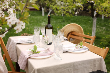 Stylish table setting with beautiful spring flowers, wine, plates and glasses in garden
