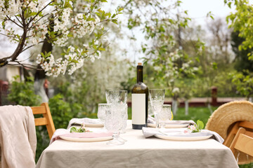 Stylish table setting with beautiful spring flowers, wine, plates and glasses in garden