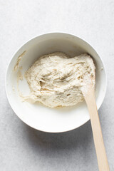 Overhead of Loosely folded bread dough, top view of high hydration dough being mixed in a white ceramic bowl