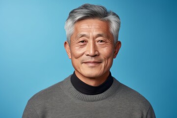 Obraz premium Portrait of a tender asian man in his 60s dressed in a warm wool sweater isolated on pastel blue background