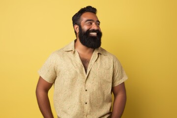 Portrait of a joyful indian man in his 30s donning a trendy cropped top while standing against pastel yellow background