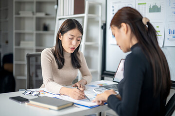 Two women are sitting at a desk, one of them writing on a piece of paper