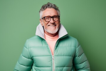 Obraz premium Portrait of a happy man in his 60s sporting a quilted insulated jacket on pastel green background