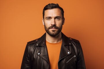 Obraz premium Portrait of a merry man in his 30s sporting a classic leather jacket in pastel orange background