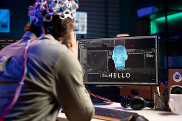 IT professional using EEG headset to communicate with artificial intelligence on computer in binary code. Software developer sending brainwave signals to AI entity on PC using high tech device