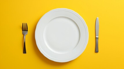 White plate with fork and knife on yellow background, shown from the top down