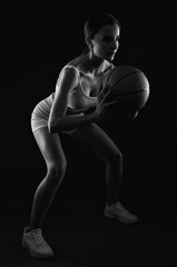 Naklejka premium A beautiful slender girl athlete in shorts and in white top plays basketball.