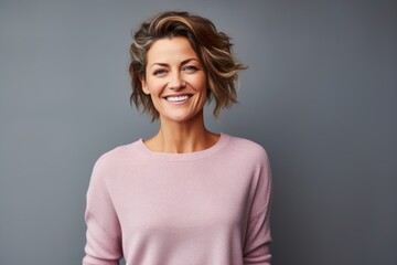 Fototapeta premium Portrait of a smiling woman in her 40s showing off a thermal merino wool top in pastel gray background