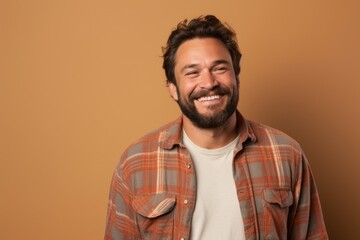 Fototapeta premium Portrait of a grinning man in his 30s wearing a comfy flannel shirt in pastel brown background