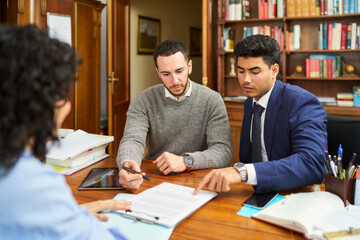 Three men are sitting at a table with papers in front of them