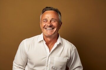 Obraz premium Portrait of a cheerful man in his 50s wearing a classic white shirt on soft brown background