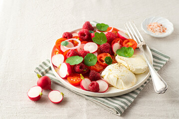 Summer salad with raspberries, cherry tomatoes, fresh radishes, mozzarella cheese and nasturtium leaves. Berries in salads, fruit salty dishes. So French. Natural cotton, farm products, summer vibes