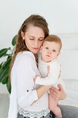 a loving mother takes care of a newborn baby, mom and baby son gently hugs and kisses at home on the bed, maternal love and care, mom plays with the baby. portrait of a happy mother with a child,