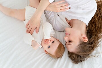 A loving mother takes care of her newborn baby son, gently hugging and kissing at home on a white bed background, maternal love and care. Portrait of a happy mother with a child, Lifestyle