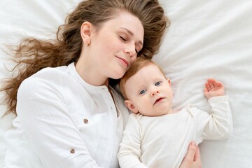 A loving mother takes care of her newborn baby son, gently hugging and kissing at home on a white bed background, maternal love and care. Portrait of a happy mother with a child, Lifestyle