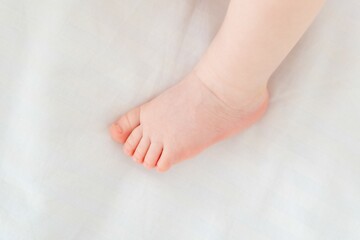 A baby's small foot on a white background of the bed, a newborn baby's heel