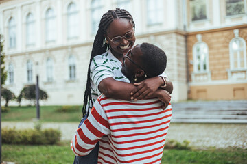 An affectionate black college couple shares a warm embrace, smiling brightly in casual campus...