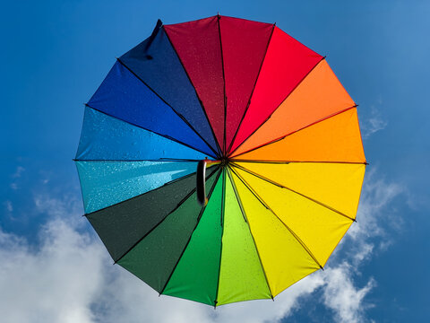 Rain Covered Multicolored Rainbow Umbrella in a Blue Sky With Clouds