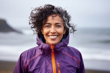 Portrait of a happy indian woman in her 50s wearing a functional windbreaker on crashing waves...