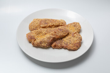 Raw breaded pork cutlets on a white plate isolated against a white background.