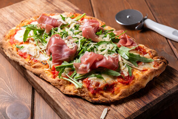 Pinsa romana condita con prosciutto crudo, rucola e scaglie di parmigiano, cibo italiano,...