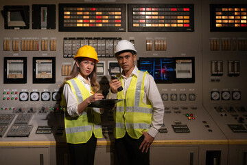 Two Asian male and female engineer presenters at a nuclear power plant stand in front of a...