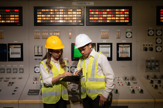 Asian male and female engineers collaborate in a nuclear power plant, brainstorming to produce energy for global export while machines and mechanisms operate in the control room.
