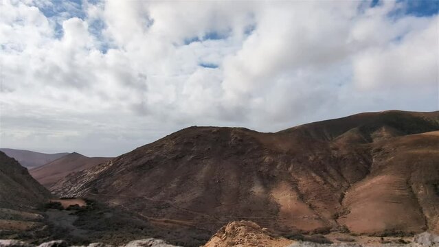 Gray clouds cast shadows as they move over the mountains of the windy island of Furteventura in the Canary Islands of Spain captured in time lapse.