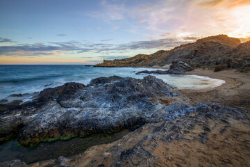 Sunset view of Minas Cove beach in Cabo Cope and Puntas de Calnegre Regional Park, with crystal clear water and rocks in the foreground
