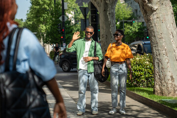 Smiling African American lovers couple meeting good friend outdoors while having joint romantic walk. Fun carefree girlfriend boyfriend strolling together outside, greeting with groupmate saying hello