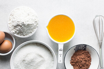 mise en place of ingredients for making brownies, top view of sugar, eggs, butter, flour cocoa powder on a marble table, process of making brownies