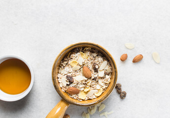 Top view of oat muesli in a brown terracotta ramekin with handle, overhead view of muesli with oats almonds raisins and cornflakes in a brown breakfast bowl, prepping healthy granola breakfast bowl