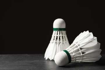 Feather badminton shuttlecocks on grey table against black background, closeup. Space for text