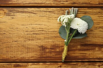 Small stylish boutonniere on wooden table, top view. Space for text