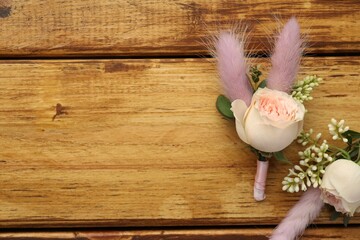 Small stylish boutonnieres on wooden table, flat lay. Space for text