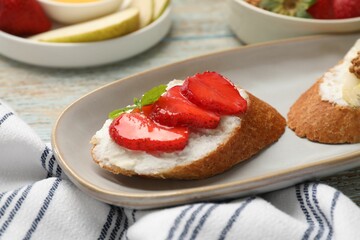 Delicious ricotta bruschettas with strawberry and mint on wooden table, closeup