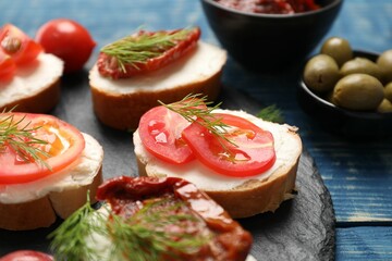 Delicious bruschettas with ricotta cheese, tomatoes, dill and olives on blue wooden table, closeup