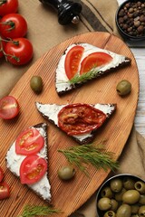 Delicious bruschettas with ricotta cheese, dill, olives, fresh and sun dried tomatoes on table, flat lay