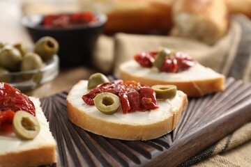 Delicious bruschettas with ricotta cheese, sun dried tomatoes and olives on table, closeup