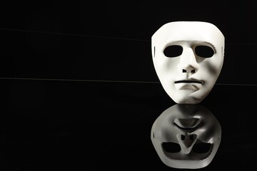 Plastic face mask on black mirror surface, space for text. Theatrical performance