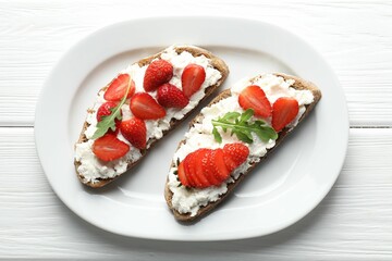 Delicious ricotta bruschettas with strawberry and arugula on white wooden table, top view