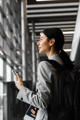 Fototapeta premium Asian girl traveler with luggage heads towards boarding gate. Business woman with backpack and smartphone waiting for departure.