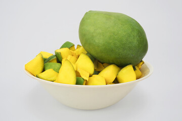 side view of mango slices with a large mango in a big white bowl, prepared for making mango pickle.