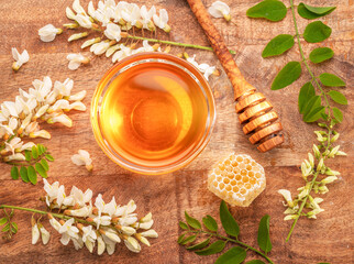 Natural organic honey in glass bowl, honey plant acacia flowers and leaves near it on wooden table. Top view.