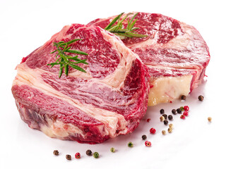 Raw beef steaks with herbs and spices ready for cooking on white background.