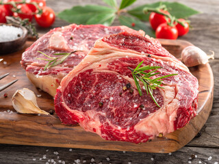 Raw beef steaks with herbs and spices ready for cooking are on wooden board.