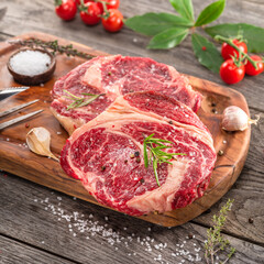 Raw beef steaks with herbs and spices ready for cooking are on wooden board.