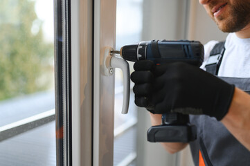 Worker installing plastic window indoors.