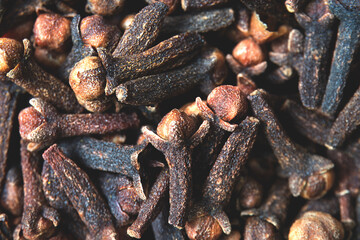 A close-up texture of freshly dried clove spices scattered on the ground. Cloves serve as a dried herb for food flavoring and natural medicine. Dry Organic Clove Spice.